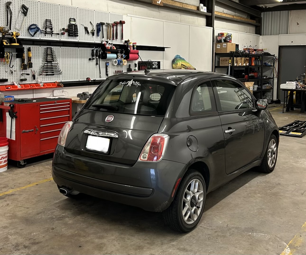 Grey Fiat 500 parked beside the organized tool wall, with its license plate obscured